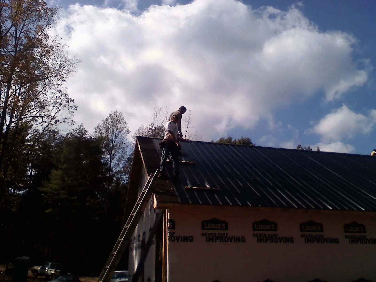 Roofer fastening dark metal panels high against a cloudy sky, from a Roof Inspection job in Wayne